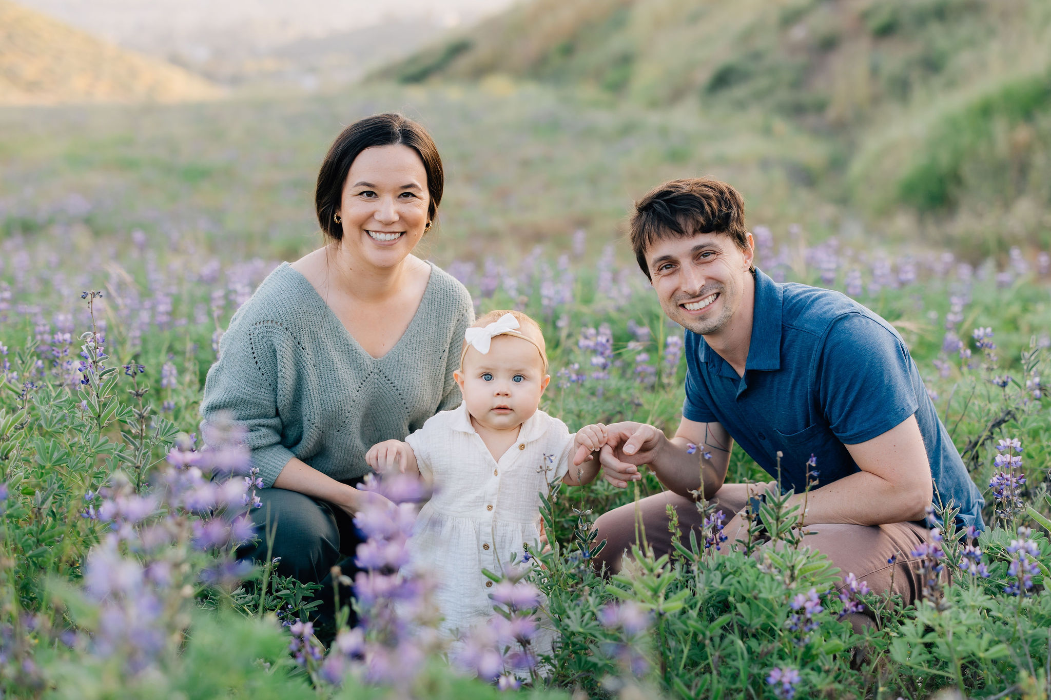 A mom and dad sit in a field of wildflowers with their toddler daughter between them before visiting baby stores in santa clarita ca