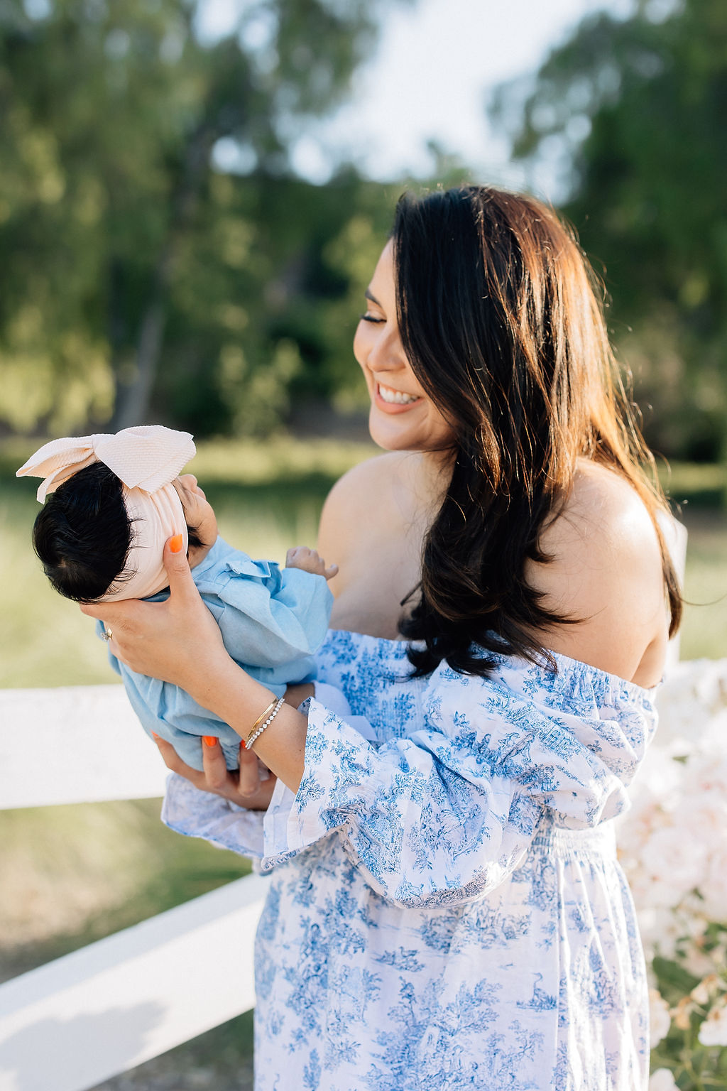 A happy new mom stands in a park smiling at her newborn baby in her hands in a blue dress after meeting a doula santa clarita