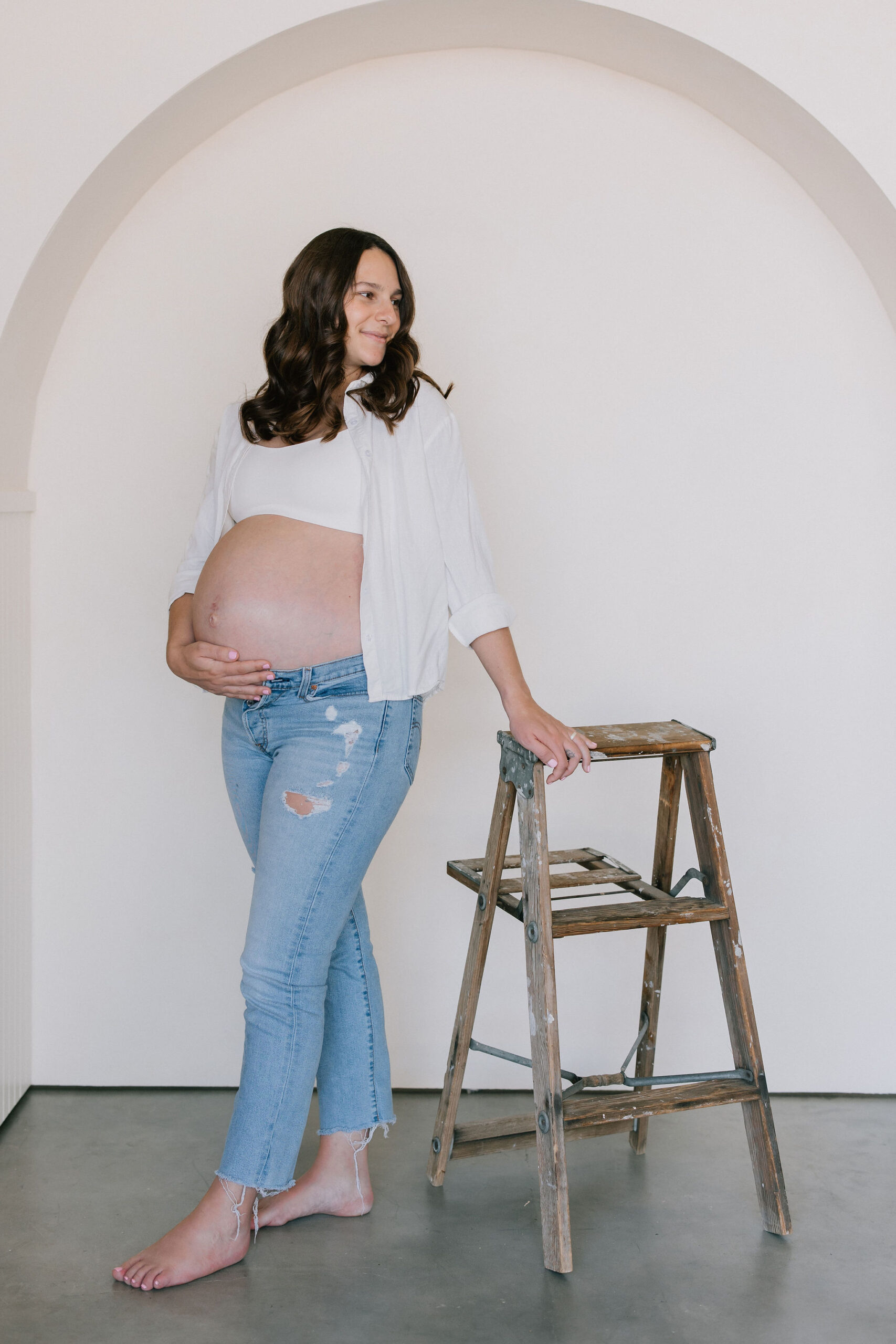 A mother to be leans on a step ladder while holding her bump in jeans and crop top after a 3d ultrasound santa clarita