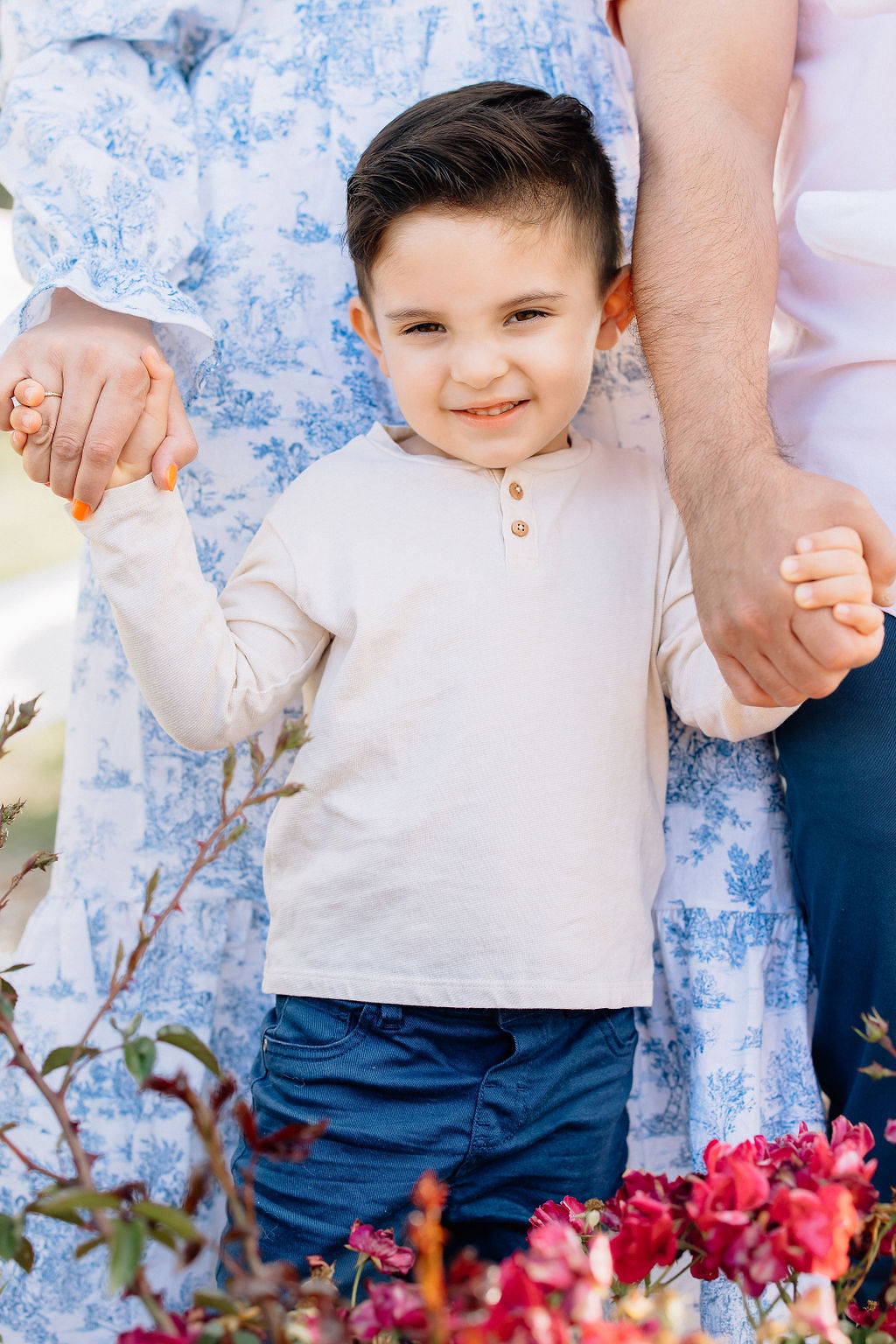 A toddler boy in a tan shirt stands in a garden holding hands with mom and dad before visiting fall festival santa clarita