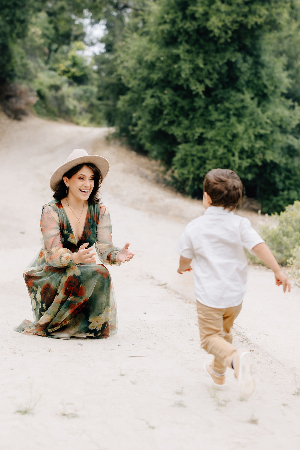 A toddler boy runs on a park path towards kneeling mom as she smiles big after visiting pediatrician santa clarita