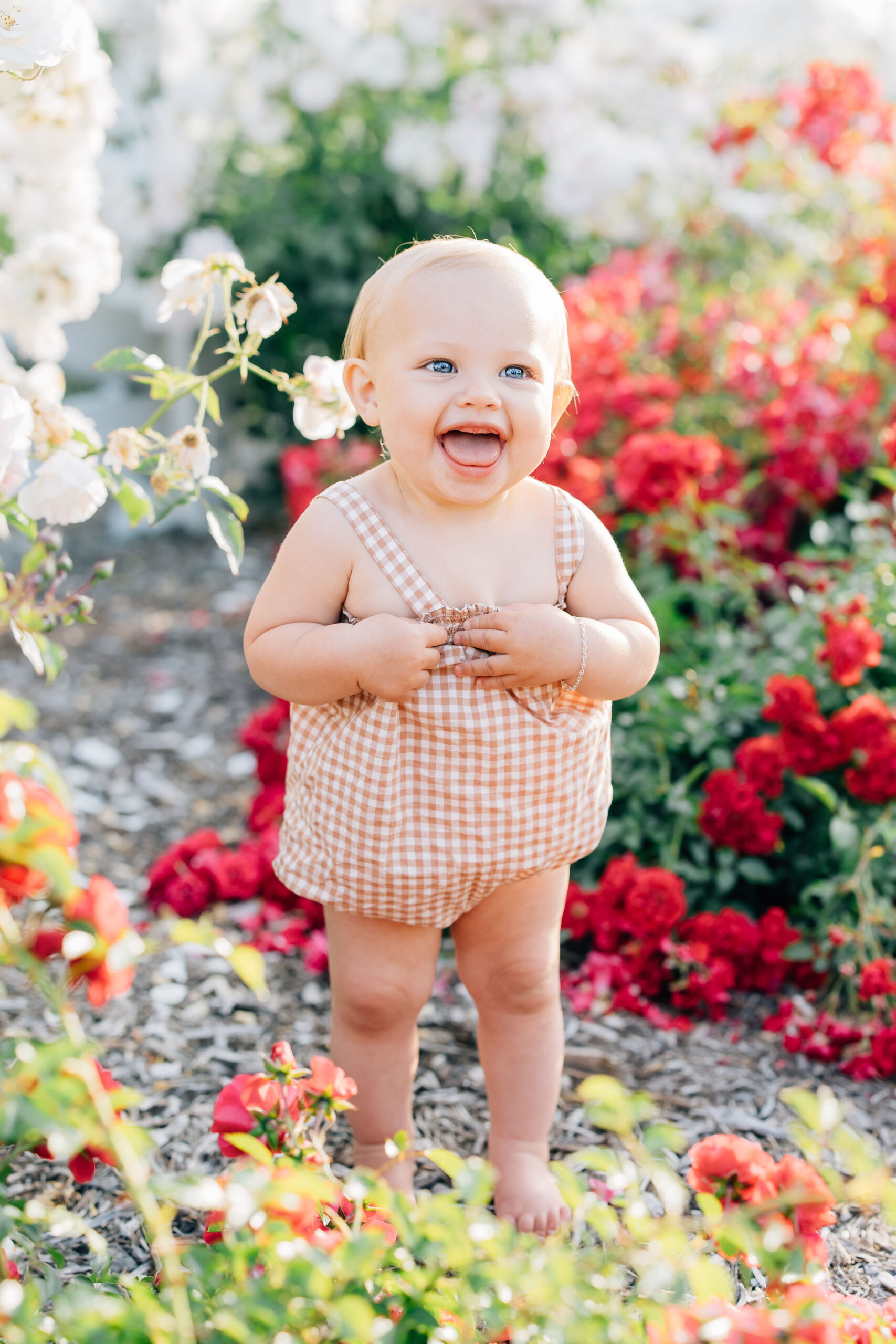 A happy toddler in an orange romper walks through a vibrant flower garden with mouth open