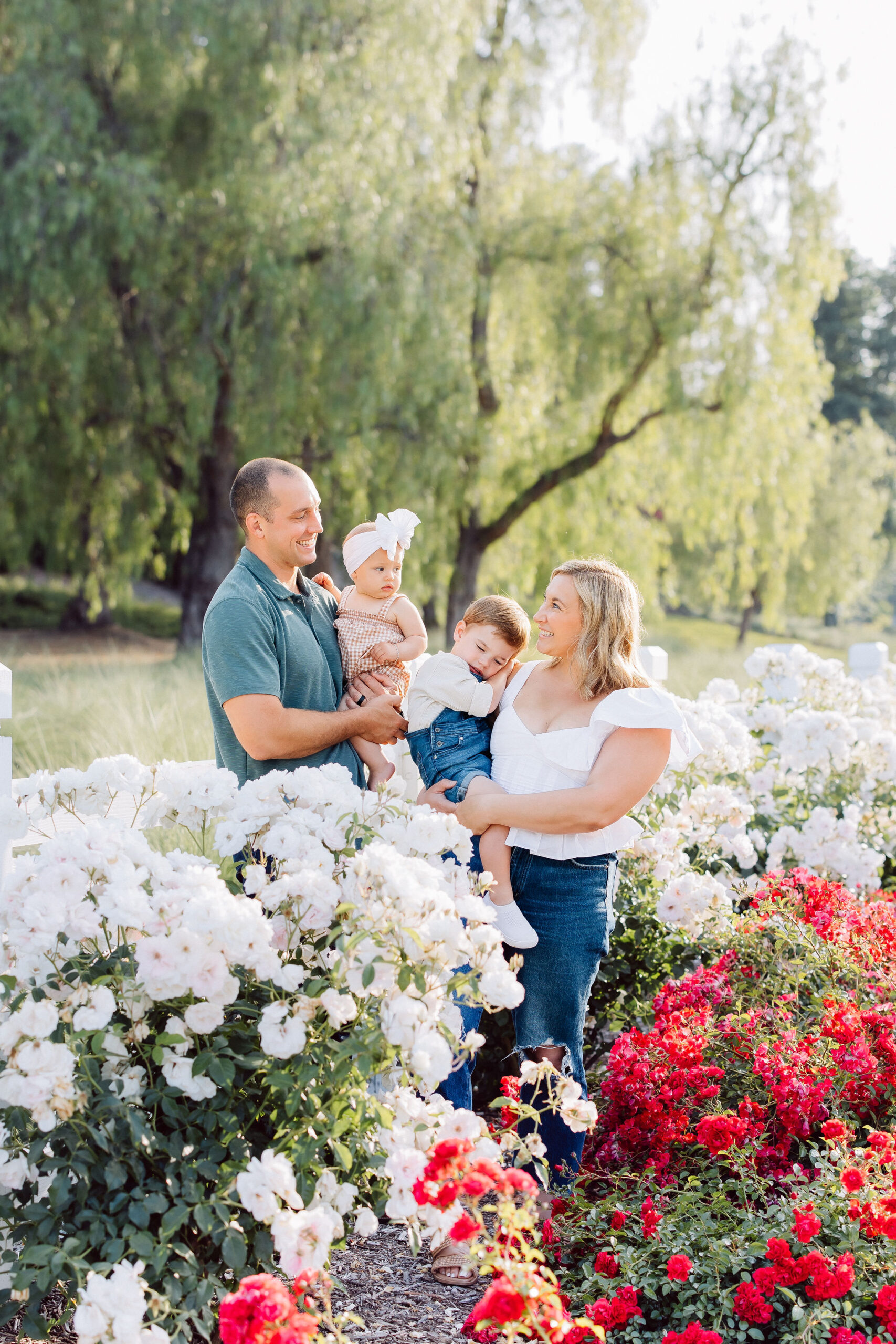 A happy mom and dad explore a vibrant flower garden with their toddler son and daughter on their hips after visiting pediatric dentist santa clarita