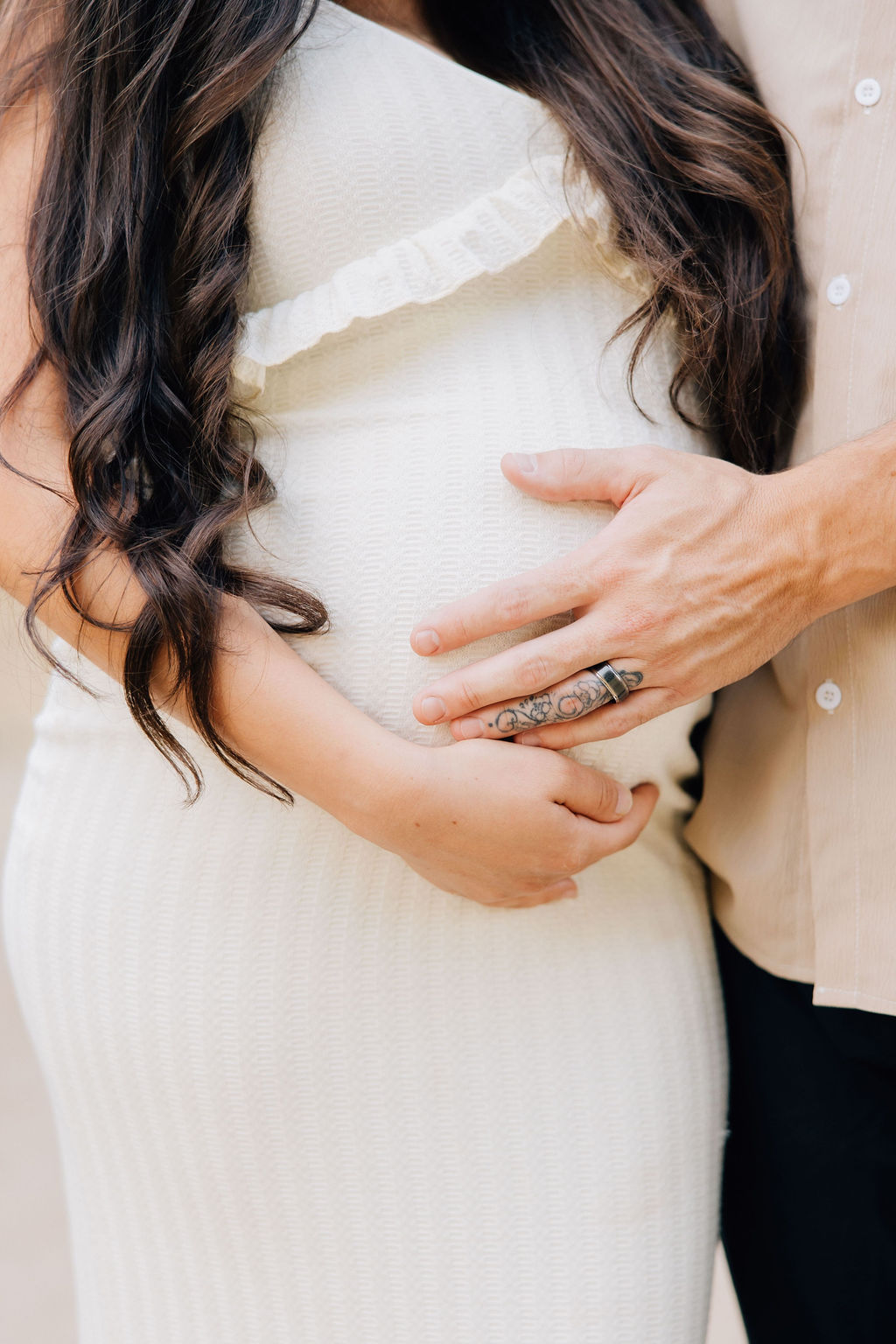 Details of expecting parents' hands on the bump in a white gown