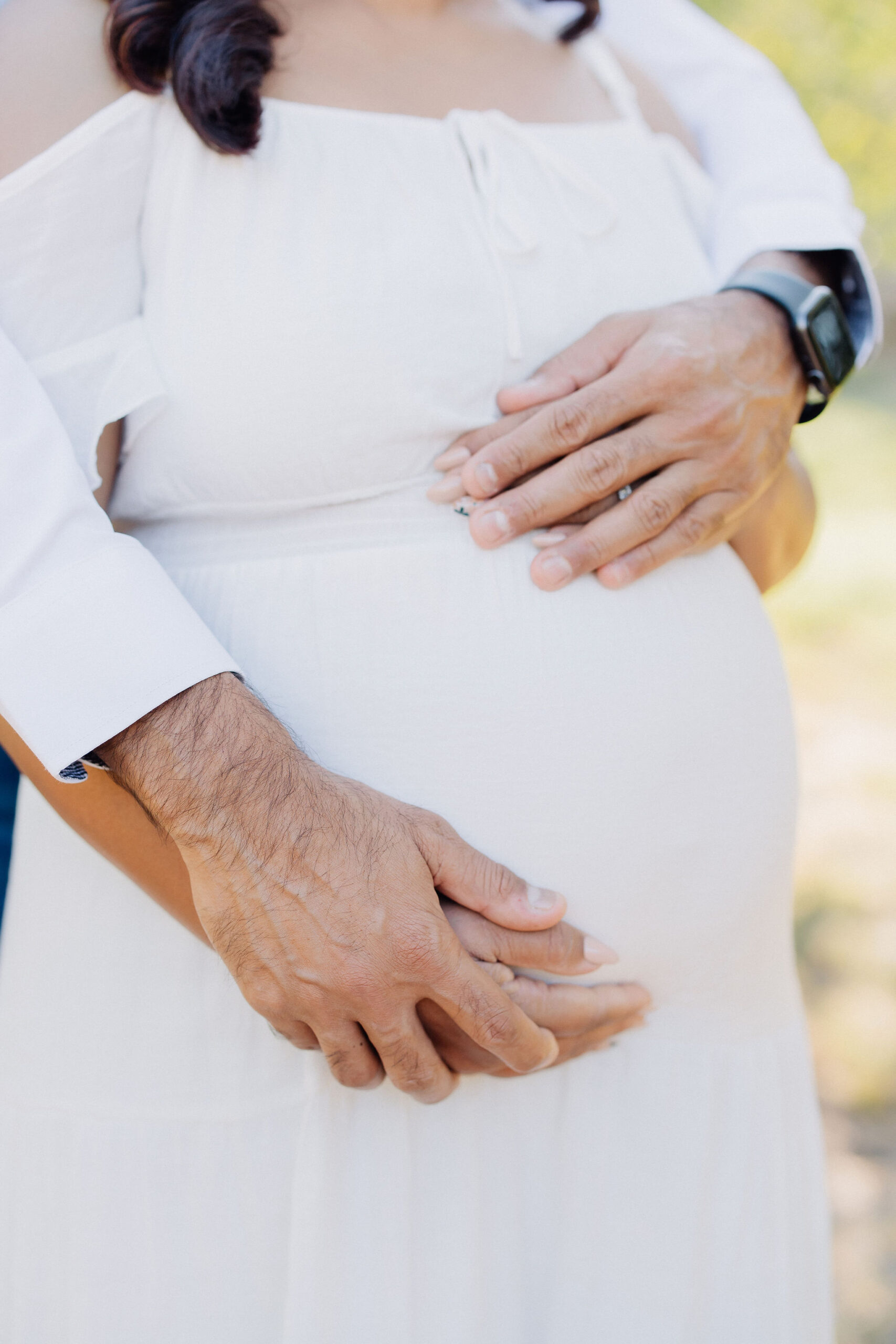 Details of expecting parents standing in a park with hands on the bump after a prenatal massage in santa clarita