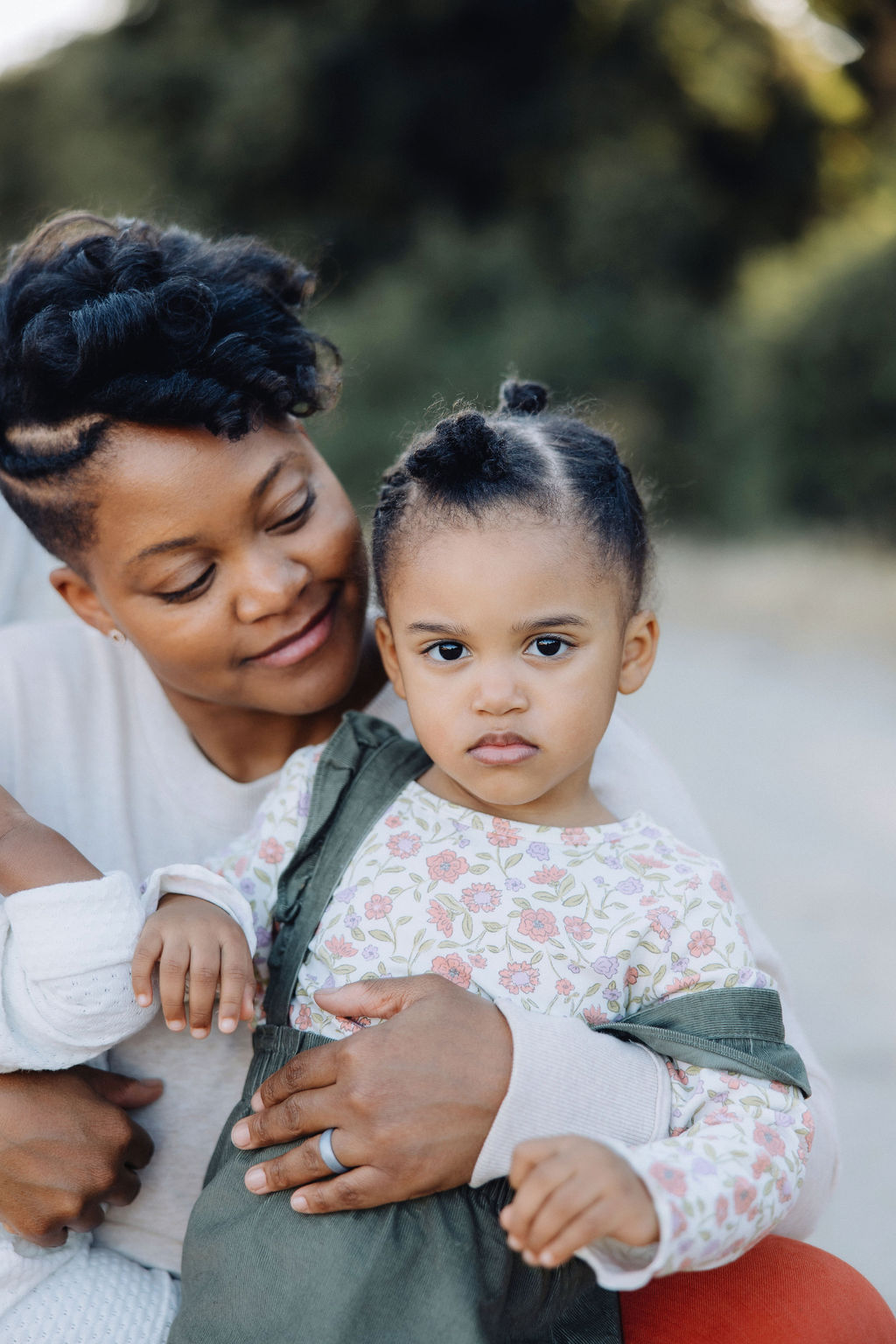 A young girl sits in mom's arms in a park as she smiles at her after some parenting classes in Santa Clarita