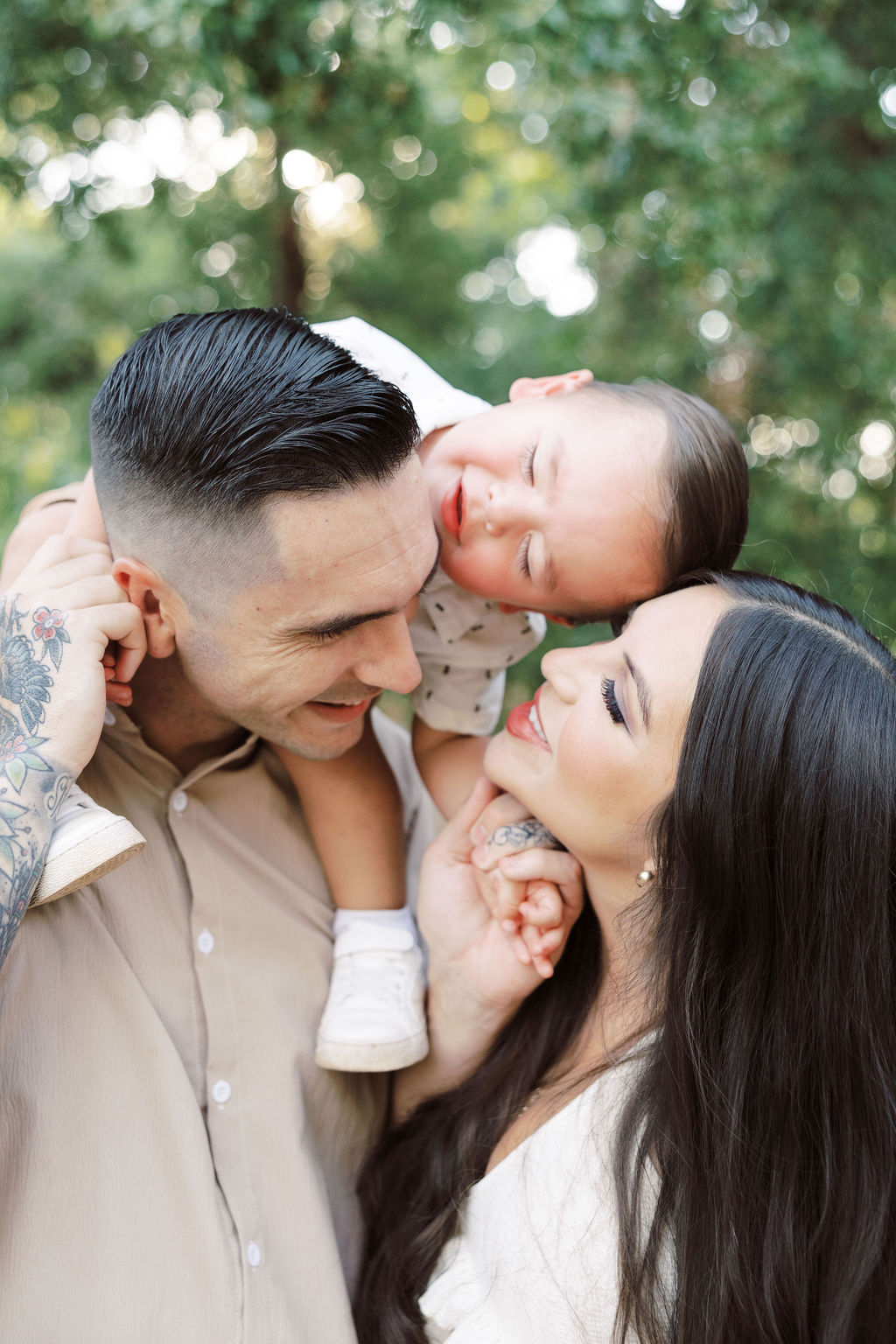 A happy family plays with baby on dad's shoulders in a park at sunset