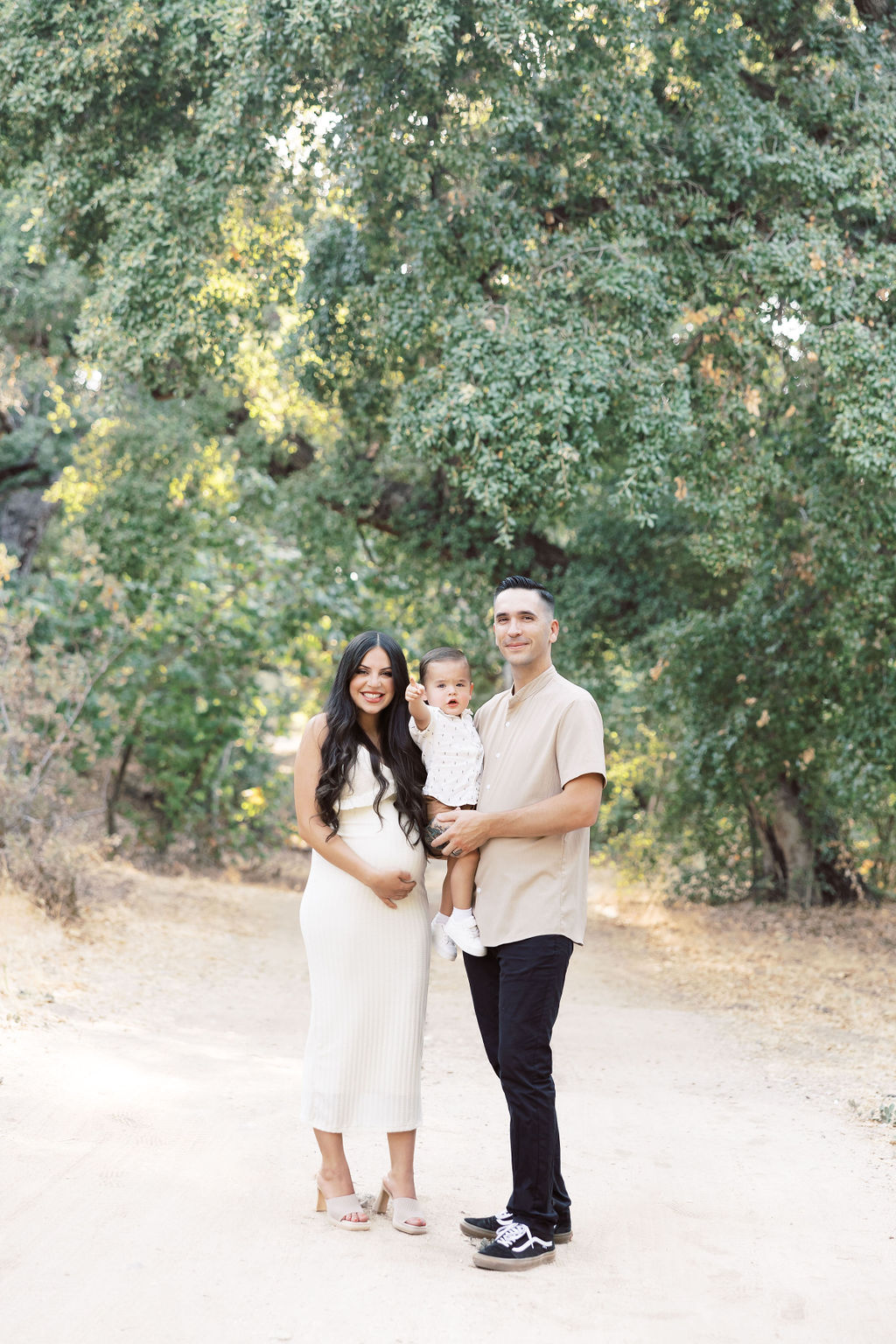 A pregnant mother stands in a park trail with her husband and baby son smiling before some pelvic floor therapy in santa clarita