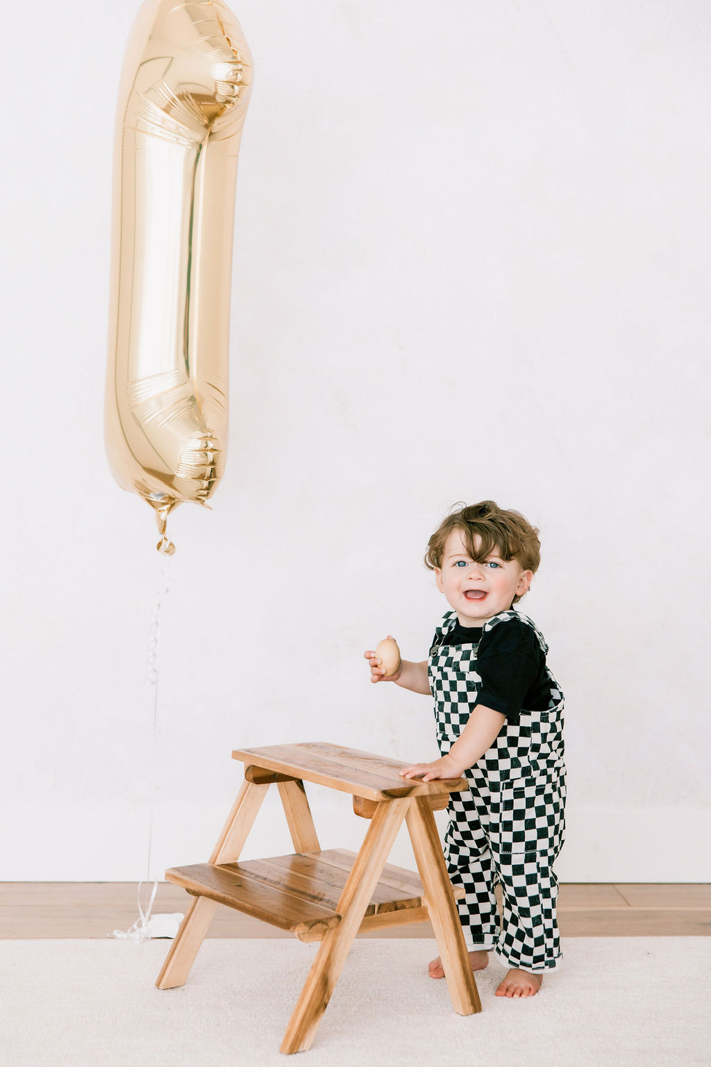 A baby in checker overalls climbs a stool in a studio before visiting preschools in Santa Clarita