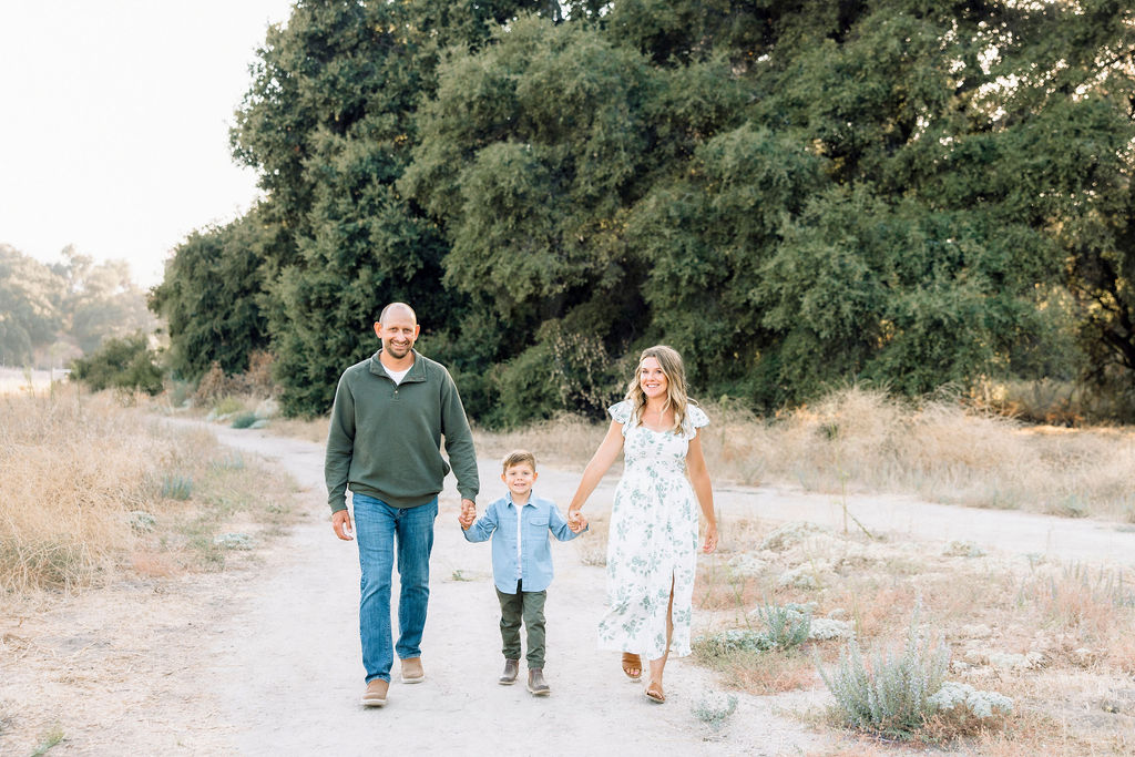 A happy young boy walks in a park trail holding hands with mom and dad at sunset after some swim lessons in Santa Clarita