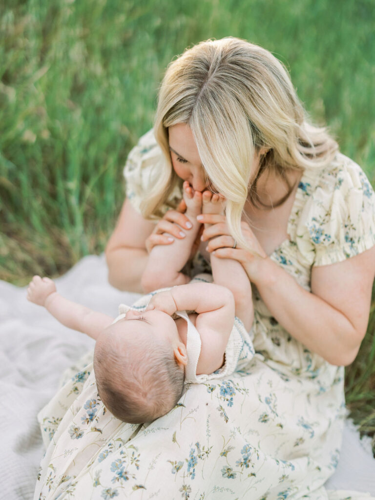 Mother kissing her baby’s feet during a tender outdoor family moment.