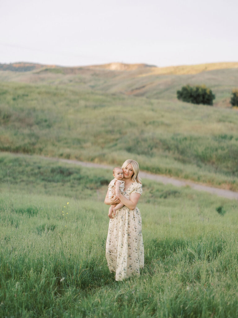 Mother holding her baby in a lush green field during a spring family photo session.