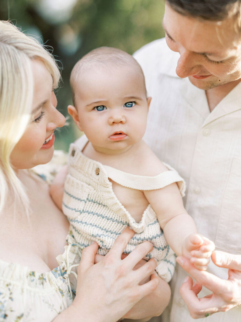 Baby looking at the camera while being held by both parents during an outdoor family session.