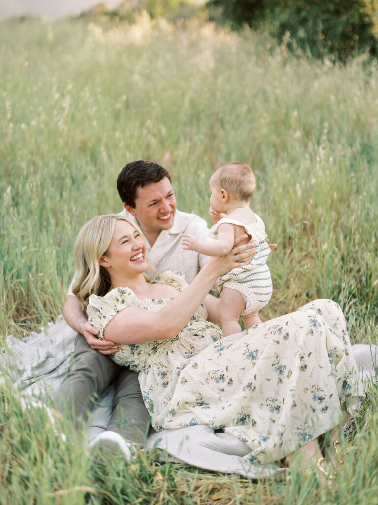Parents laughing with their baby during a relaxed outdoor family photo session.