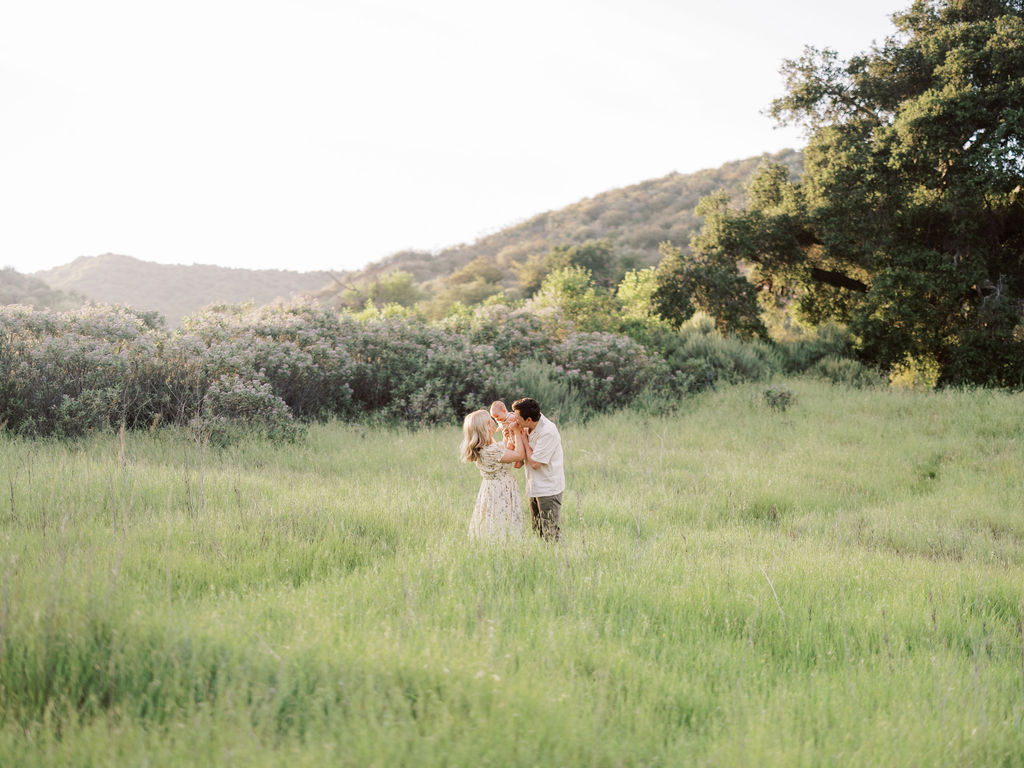 Parents sharing a sweet moment with their baby in a sunlit field during a family photo session.