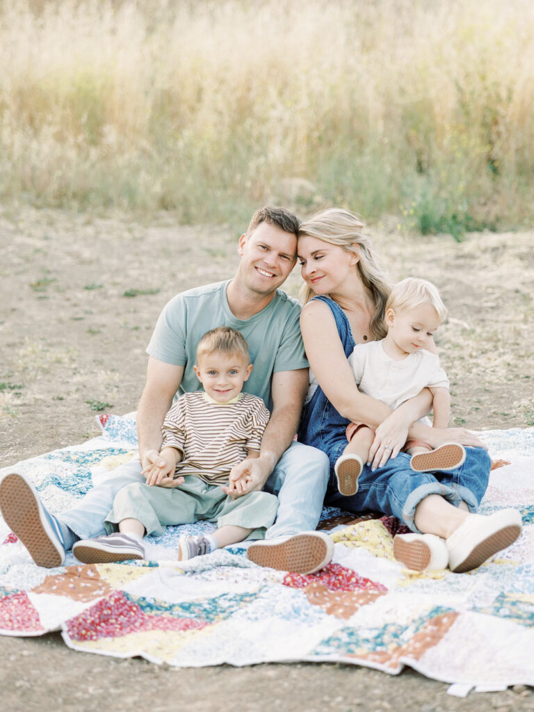 Family of four sitting together on a quilt with two young children during relaxed family photos with toddlers in Santa Clarita.