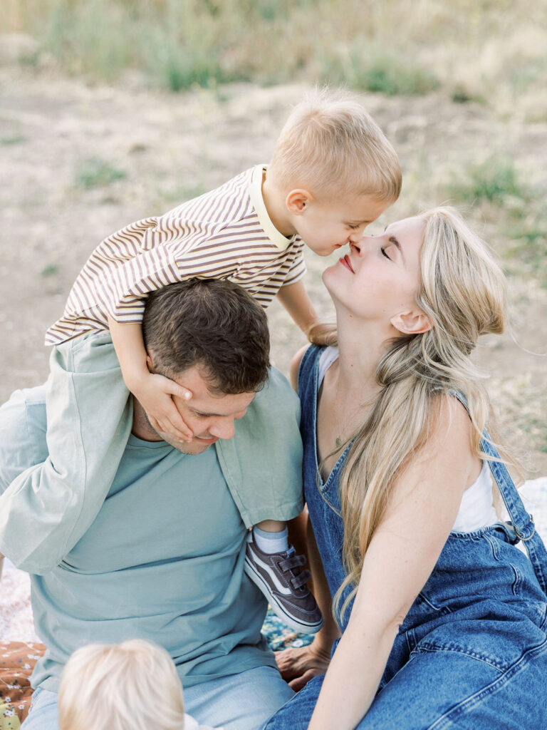 Toddler leaning down to kiss mom while sitting on dad’s shoulders during playful family photos with toddlers in Santa Clarita.