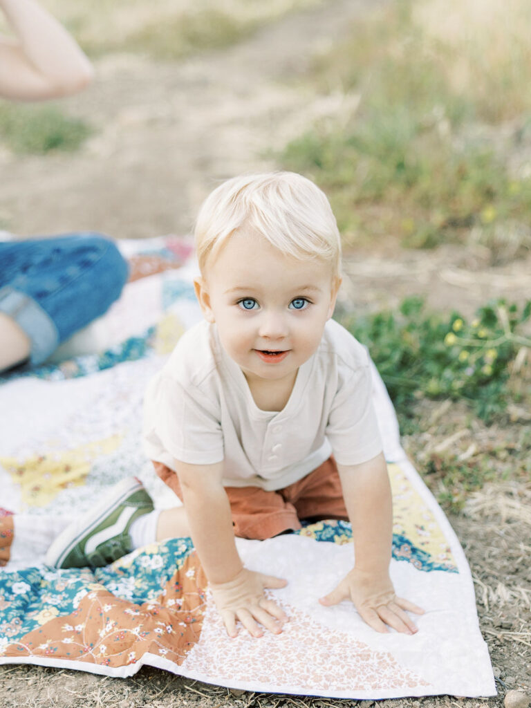 Toddler crawling on a colorful quilt and looking at the camera during a playful Santa Clarita family photo session.