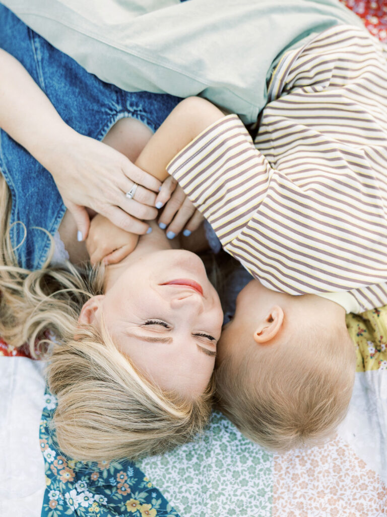 Toddler snuggling close to mom while they lie together on a colorful quilt during natural family photos with toddlers in Santa Clarita.
