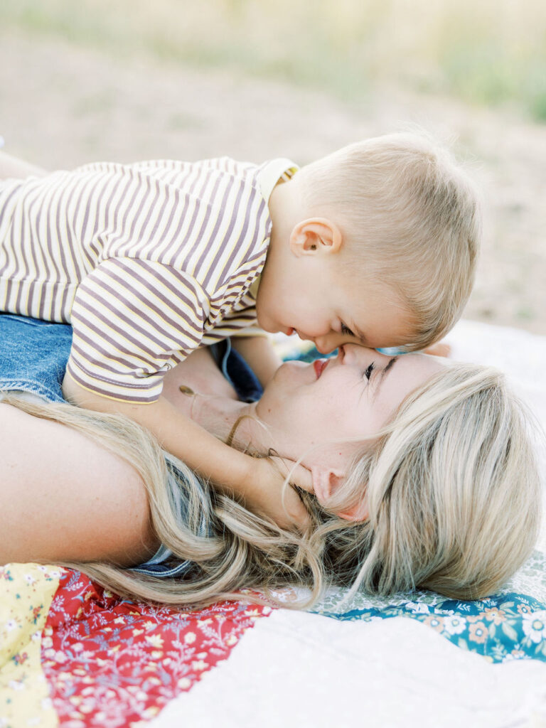 Toddler leaning over mom for a playful kiss while they lie on a quilt during natural family photos with toddlers in Santa Clarita.