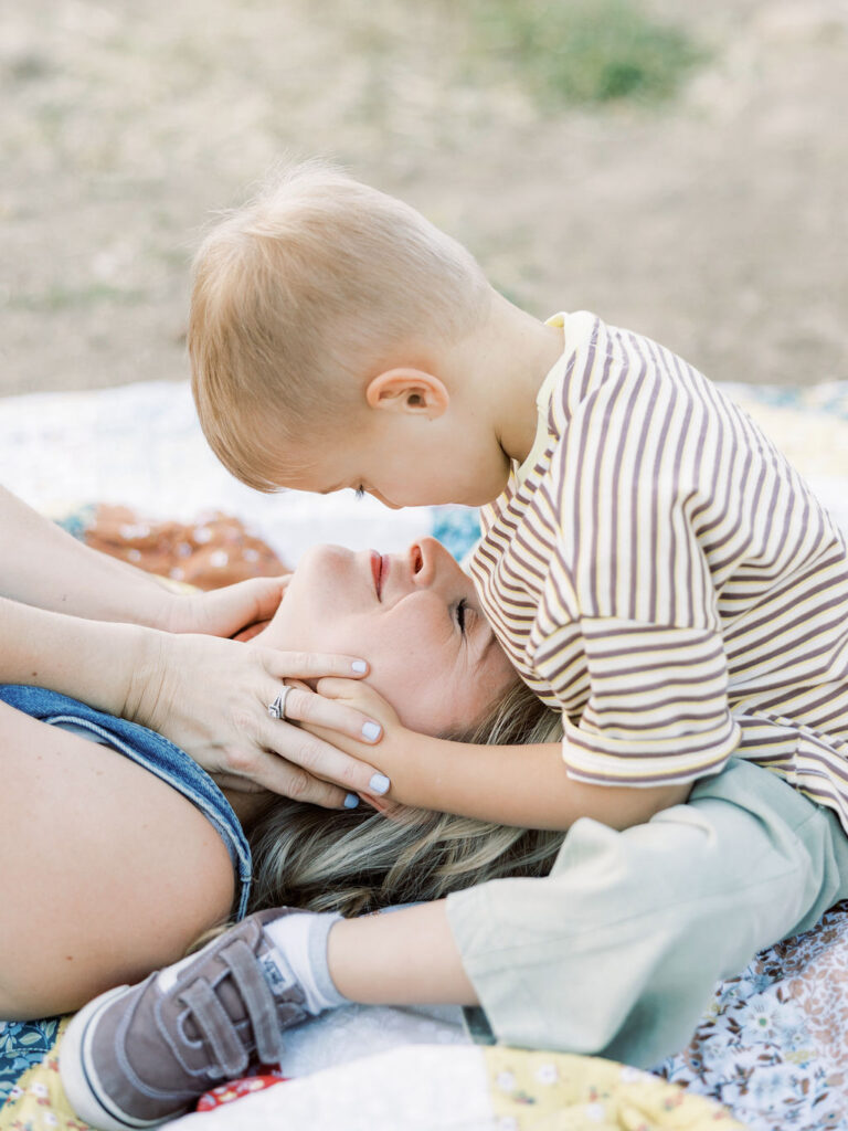 Toddler sitting over mom and gently holding her face during playful family photos with toddlers in Santa Clarita.