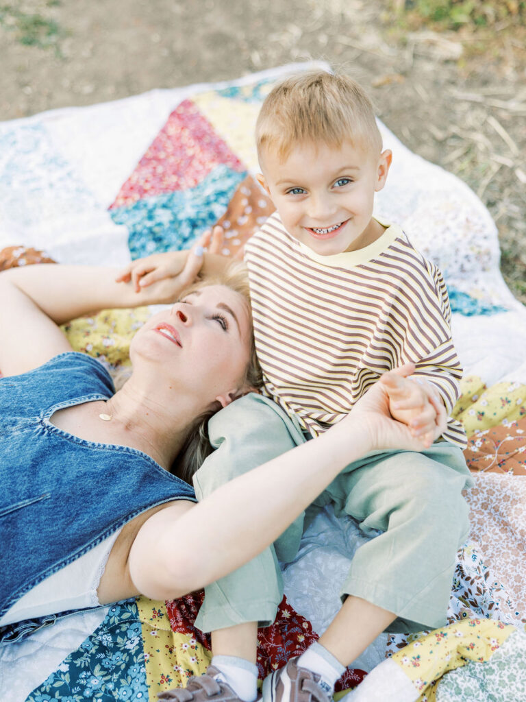 Toddler sitting beside mom on a colorful quilt while they hold hands during relaxed family photos with toddlers in Santa Clarita.