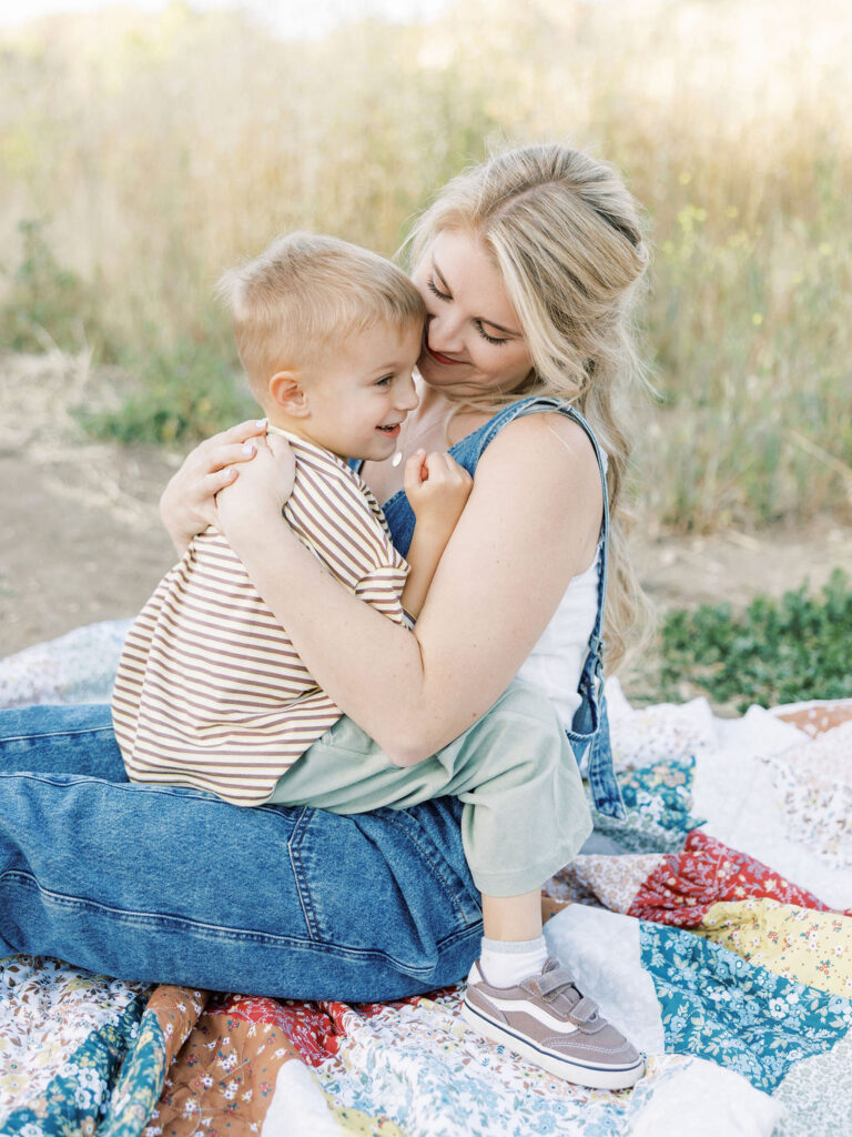 Mom cuddling her smiling toddler on a colorful quilt during natural family photos with toddlers in Santa Clarita.