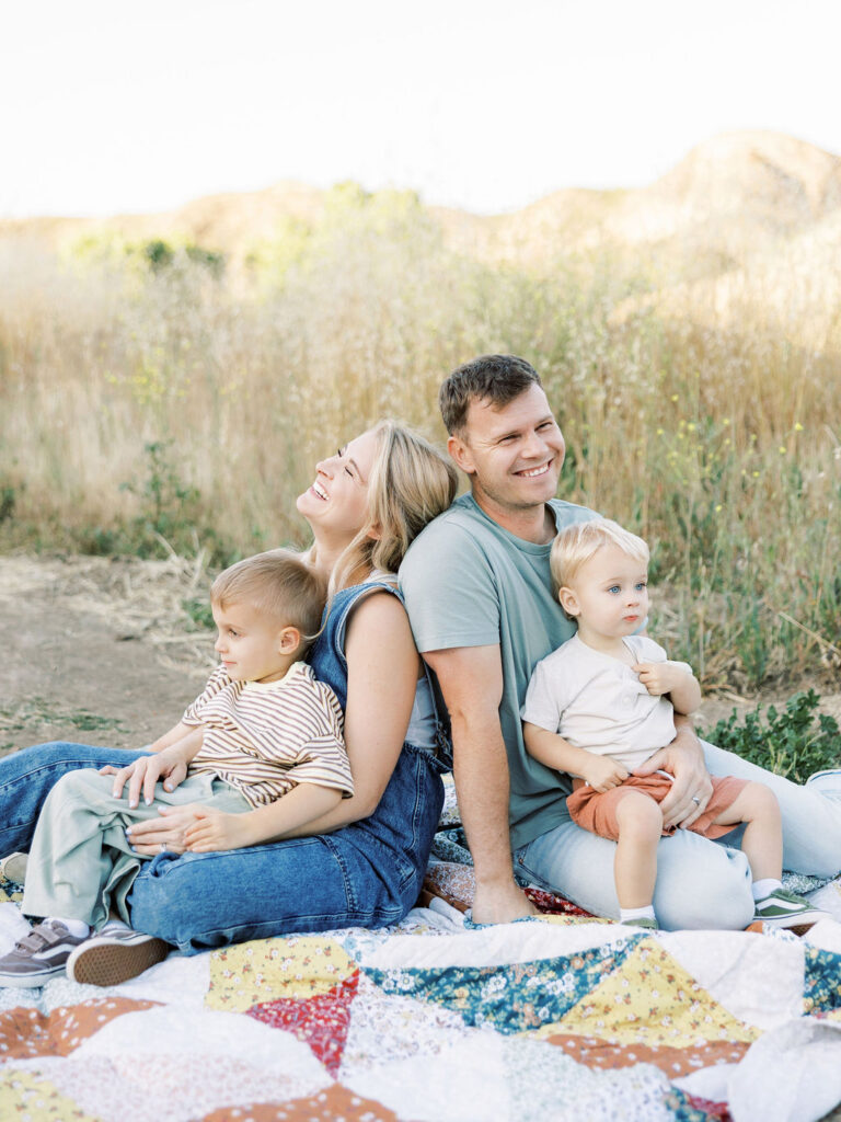 Family of four sitting together on a quilt with two young children during relaxed family photos with toddlers in Santa Clarita.
