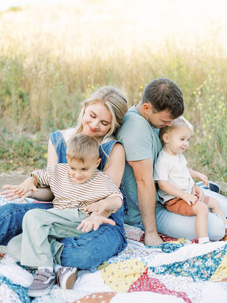 Family sitting together on a colorful blanket outdoors with their toddler during natural Santa Clarita family photos