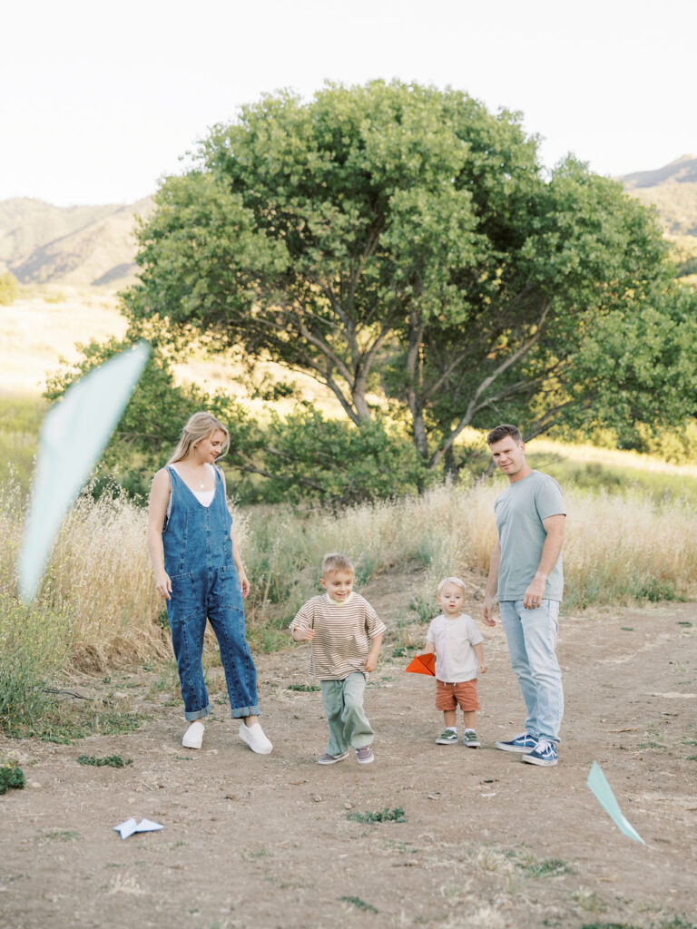 Family of four playing with paper airplanes outdoors with two young children during a relaxed Santa Clarita family photography session.