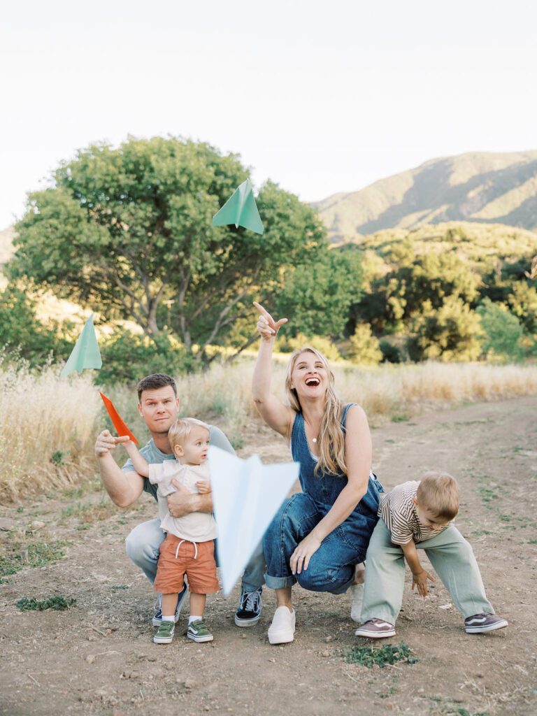 Family of four playing with paper airplanes outdoors during a fun and candid Santa Clarita family photography session.