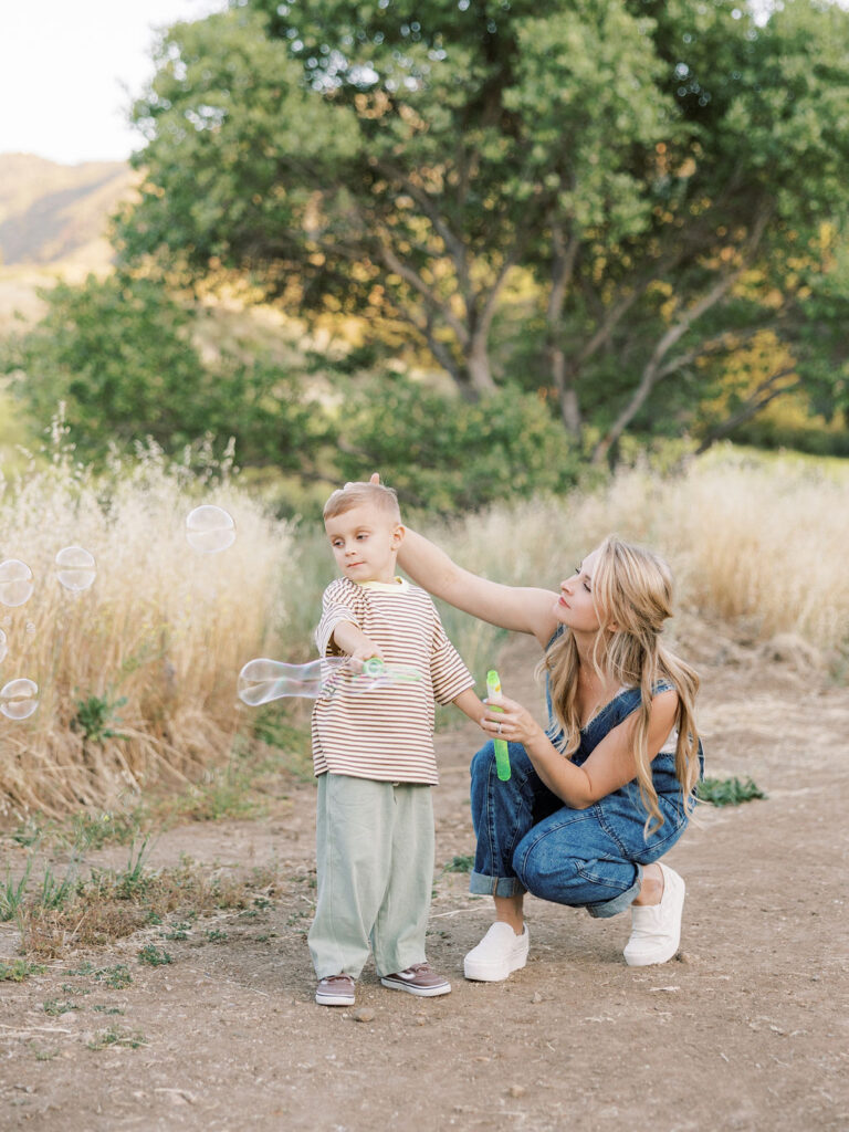 Mom helping her toddler blow bubbles outdoors during playful family photos with toddlers in Santa Clarita.