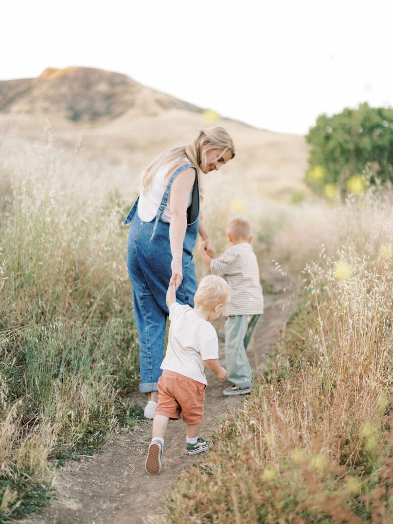 Mom and her two toddlers walking through tall grass during natural family photos in Santa Clarita