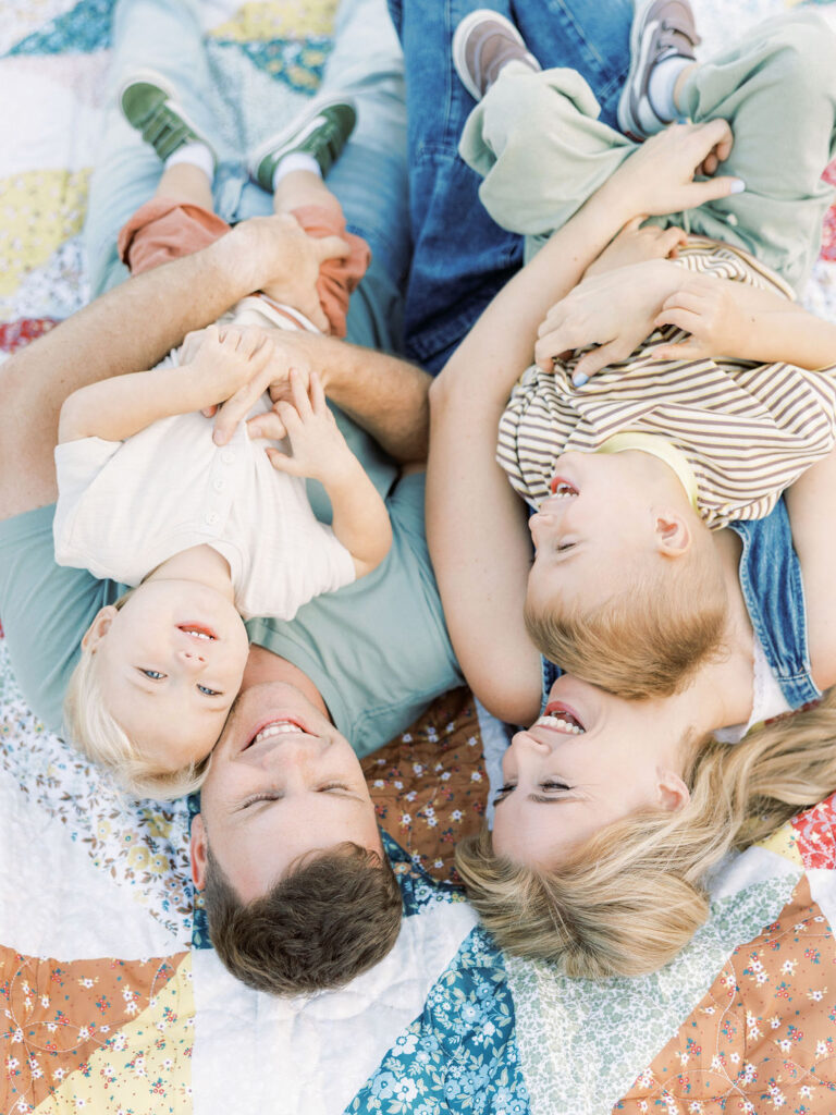 Mom and dad cuddling their toddler while lying together outdoors during a natural family photography session