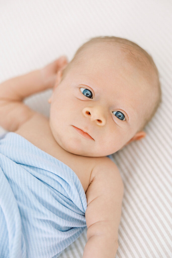 Close-up of a newborn resting on a light blanket with one hand near the face.