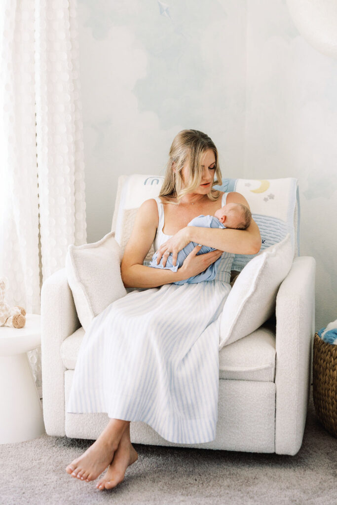Mom cuddling her baby in a nursery chair during an at-home newborn session.