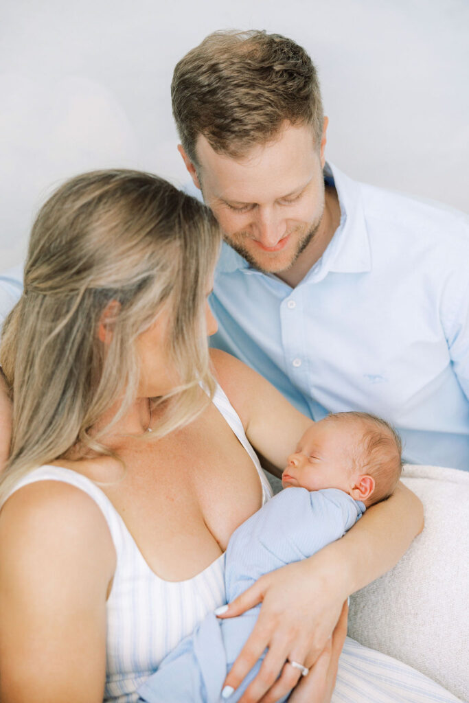 Dad gently kissing his newborn while mom holds the baby.