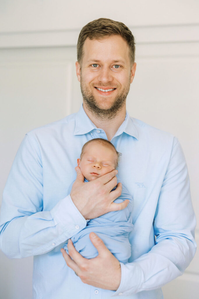 Smiling dad holding his newborn during a relaxed at-home newborn session.
