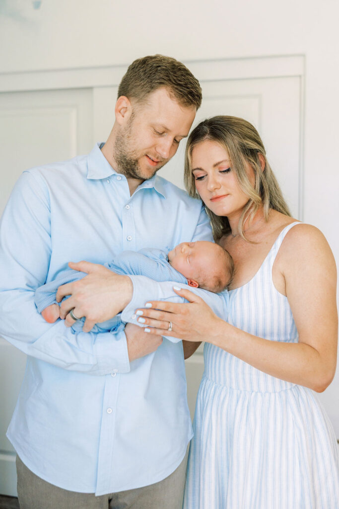 New parents standing together and cuddling their newborn at home.
