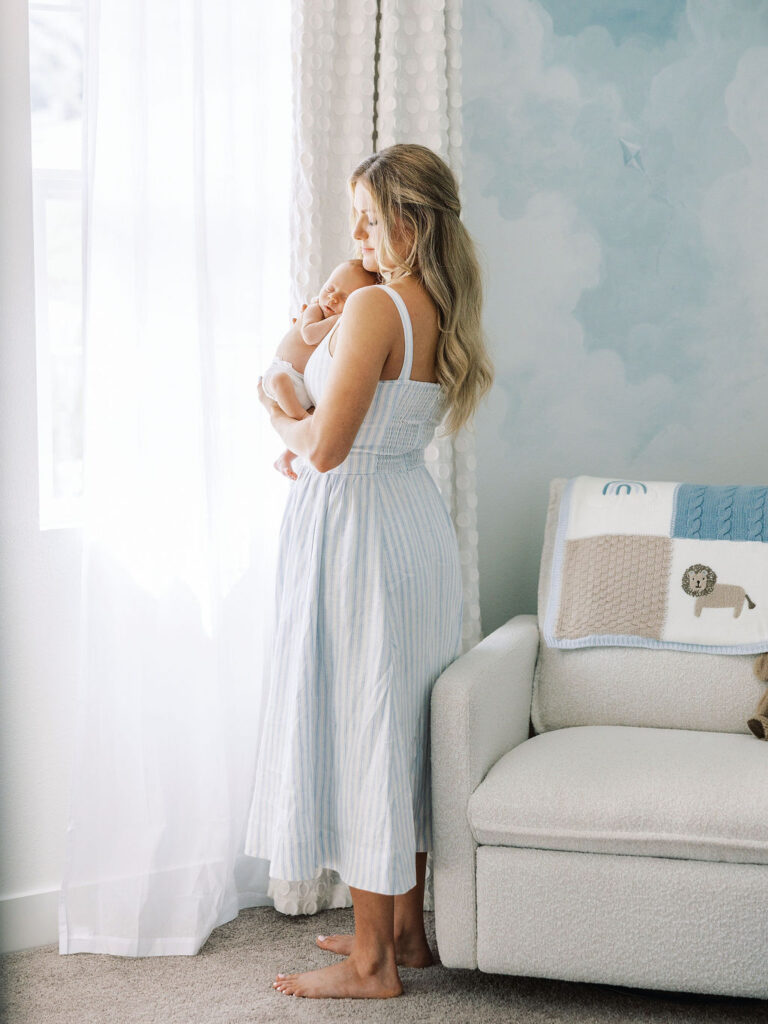 Mom standing with her newborn beside the nursery crib.