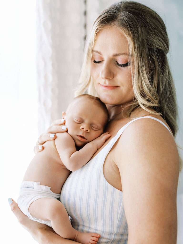 Mother holding her sleeping newborn close with her eyes closed.