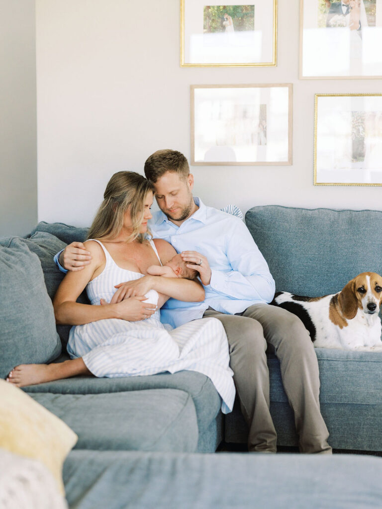 New parents cuddling their newborn on the couch with their dog during in-home newborn photography Santa Clarita.