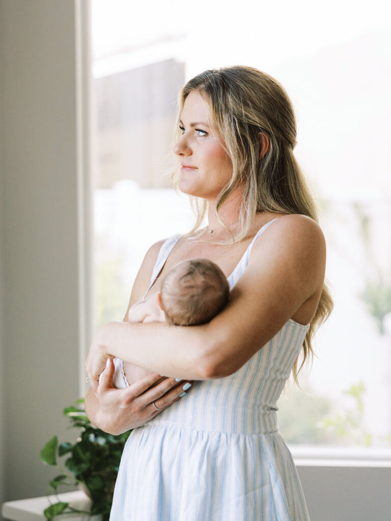 Mom holding her baby near the window during in-home newborn photography Santa Clarita.