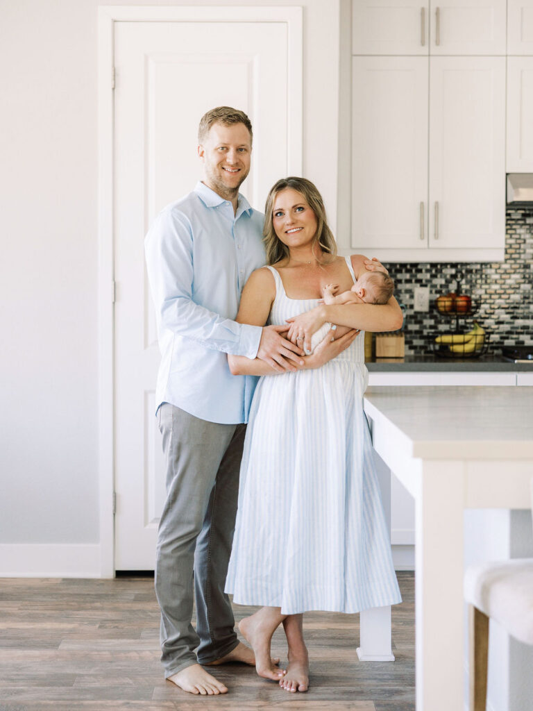 Mom and dad standing together with their newborn during an in-home newborn session.