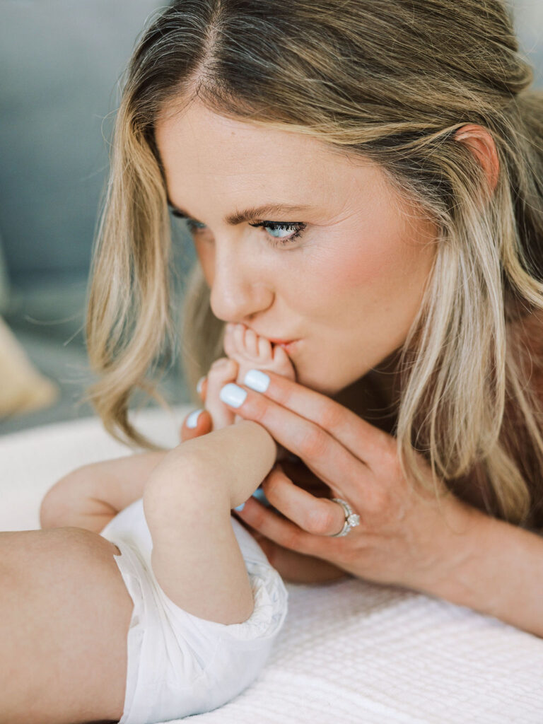 Mom kissing her newborn’s tiny hand during a lifestyle newborn session.