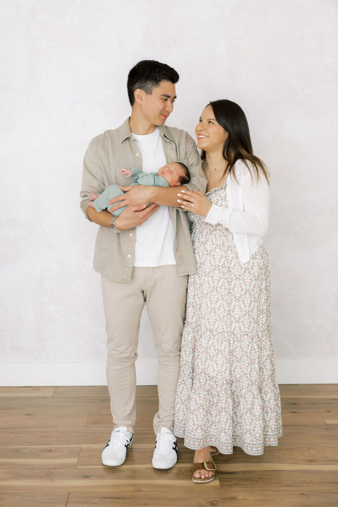 New parents standing together and holding their newborn baby in the studio