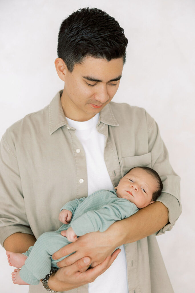 Dad looking down at his newborn baby while holding them during a relaxed studio newborn session.