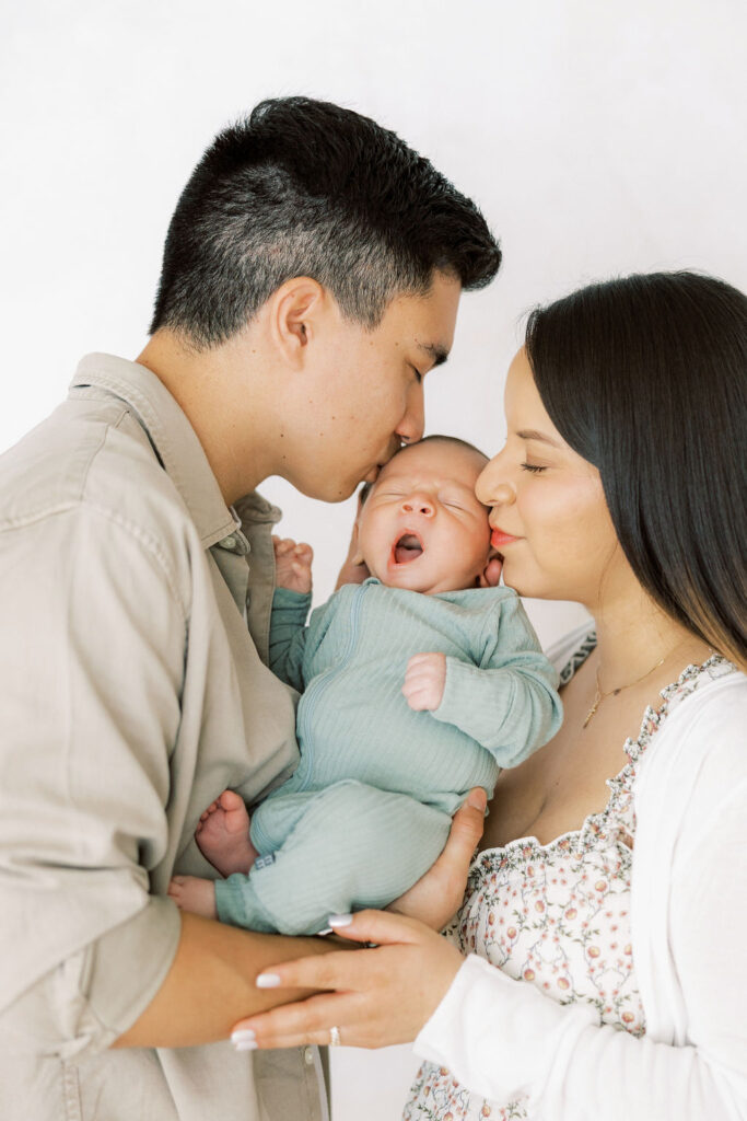 Mom and dad kissing their newborn baby during a sweet family moment