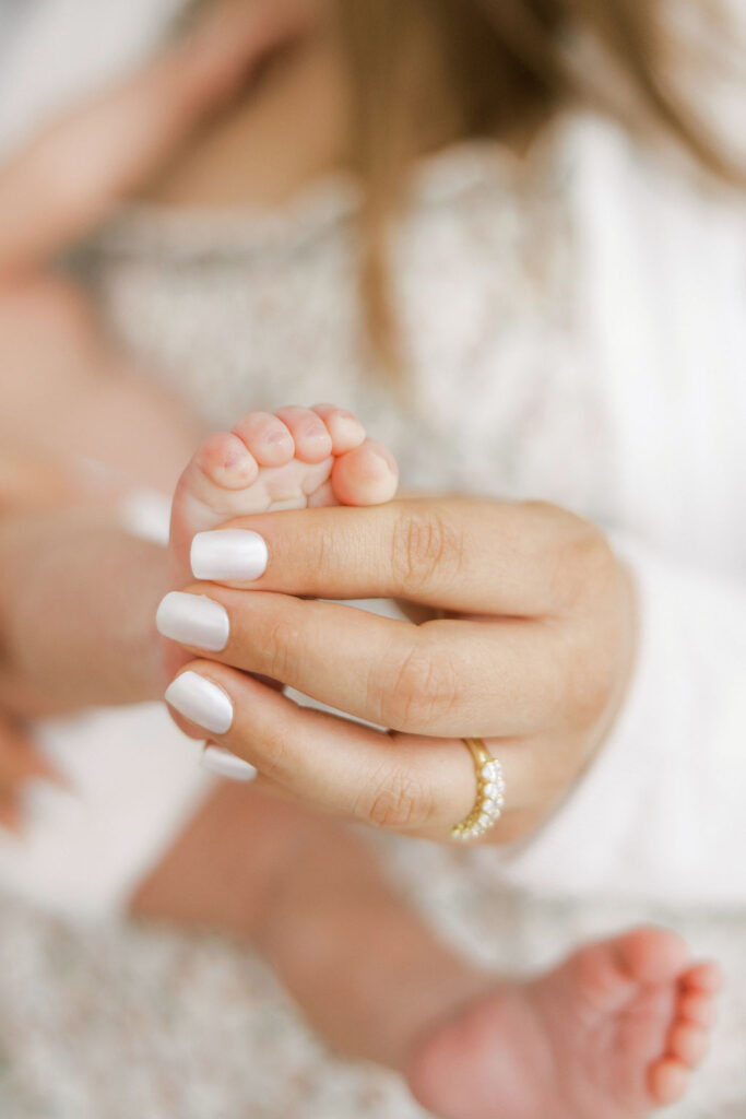 Close up of tiny newborn toes held gently in a parent’s hands