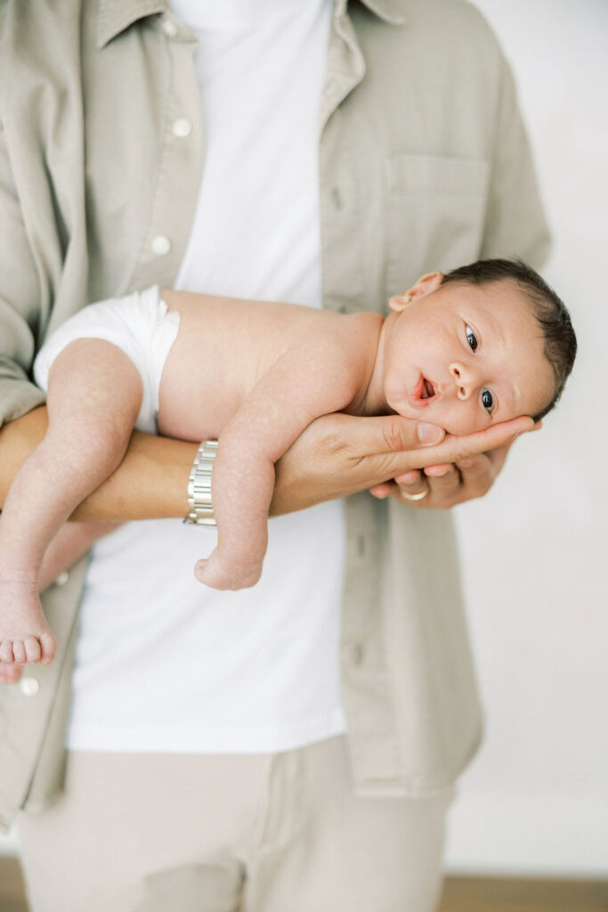 Newborn baby resting in dad’s hands during a relaxed studio newborn photography session.